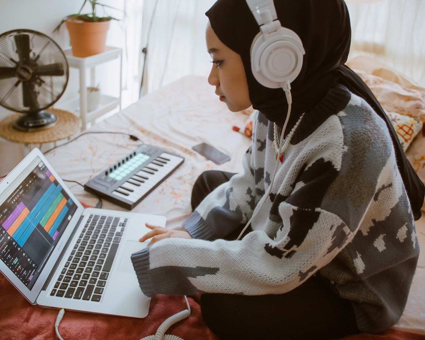 Perempuan berhijab bekerja dengan laptop di kamarnya